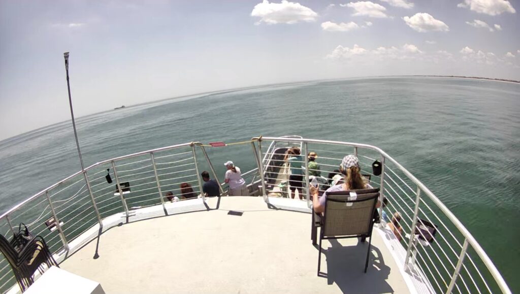 View from the VIP seating area on the upper deck of the Jersey Girl whale-watching boat, overlooking calm ocean waters and passengers watching for whales on a sunny day.